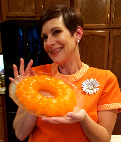 Kristi, wearing an orange shirt, smiling and holding up her orange Jello dish