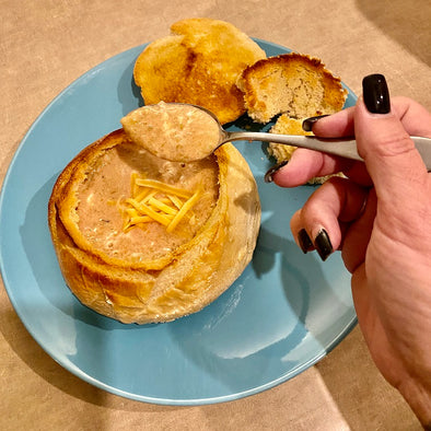 Steph's hand holding a spoonful of the pink green goddess soup, over a sourdough bread bowl filled with pink green goddess soup