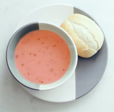 A bowl of pink green goddess soup on a plate with a roll 