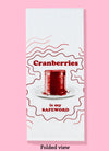 The folded "cranberries are my safeword" dishtowel. The towel features the phrase in dark read, with an illustration of uncanned cranberry sauce. There are illustration lines around the image.