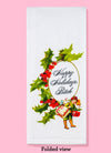The Happy Holidays Bitch dish towel shown folded. It features the text "Happy Holidays, Bitch" in a cursive type font. The text is surrounded by a golden oval, with mistletoe surround it. There is also a small illustration of a boy holding large presents.