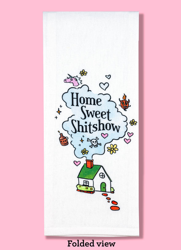 Folded dishtowel with an illustration of a small cottage with hearts, devils, unicorns, stars, and booze coming out of the chimney along with the words Home Sweet Shitshow