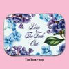 The top of the Dank tin, showing design elements of flowers on a white background with blue text that reads "Keep The Fuck Out"
