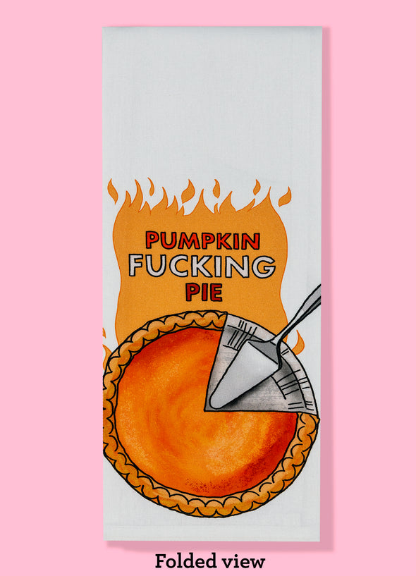 The folded view of the "Pumpkin Fucking Pie" tea towel. It features the phrase in large capital letters surrounded by illustrated flames. There is also an illustration of a pumpkin pie that has been partially cut with a serving knife.