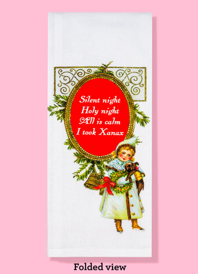 Folded view of of the Silent Night dish towel. The text is white on a red background, reading "Silent night holy night all is calm I took Xanax". The design features classic Christmas elements, along with an illustration of a child in a blue coat holding a puppy.