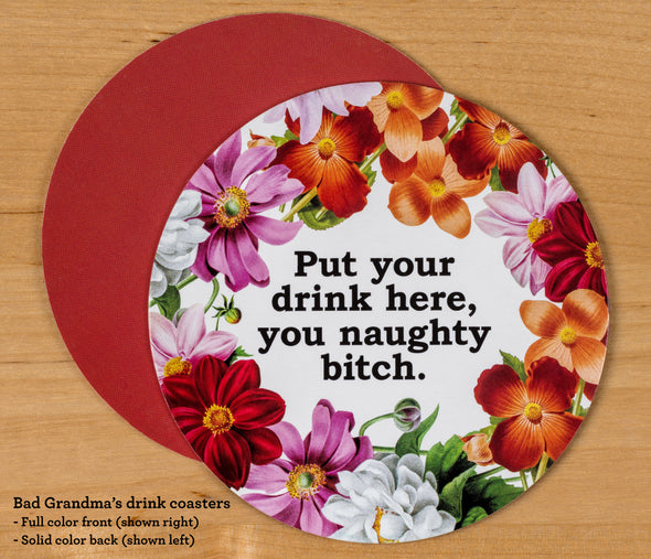 The front and back of the round drink coaster. The front features the text Put Your Drink Here You Naughty Bitch and vintage flower illustrations. The back of the coaster is russet red, which matches one of the flowers on the front.