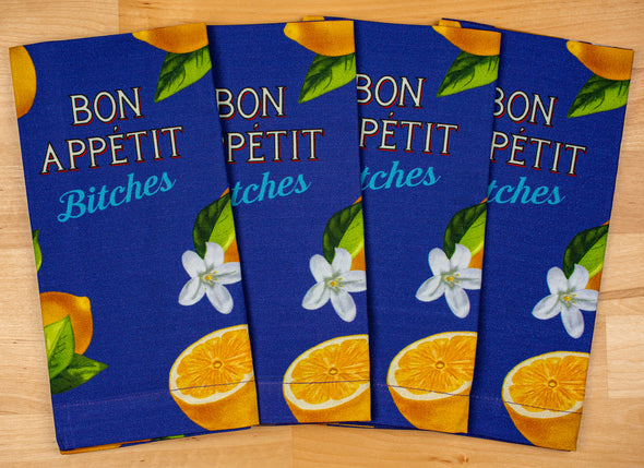 A complete set of four identical napkins. They read bon Appetit bitches. They are all folded in the same manner of the same design. 