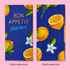 A side by side comparison of the front and back of the napkin when it is folded into eighths. The front displays the text Bon Appetit Bitches; the back shows some of the illustrated lemons and lemon flowers
