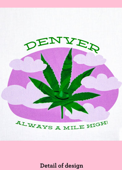Close up of a dishtowel with a smiling marijuana leaf illustration  and the phrase Denver Always a Mile High.