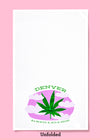 Unfolded dishtowel with a smiling marijuana leaf illustration  and the phrase Denver Always a Mile High.