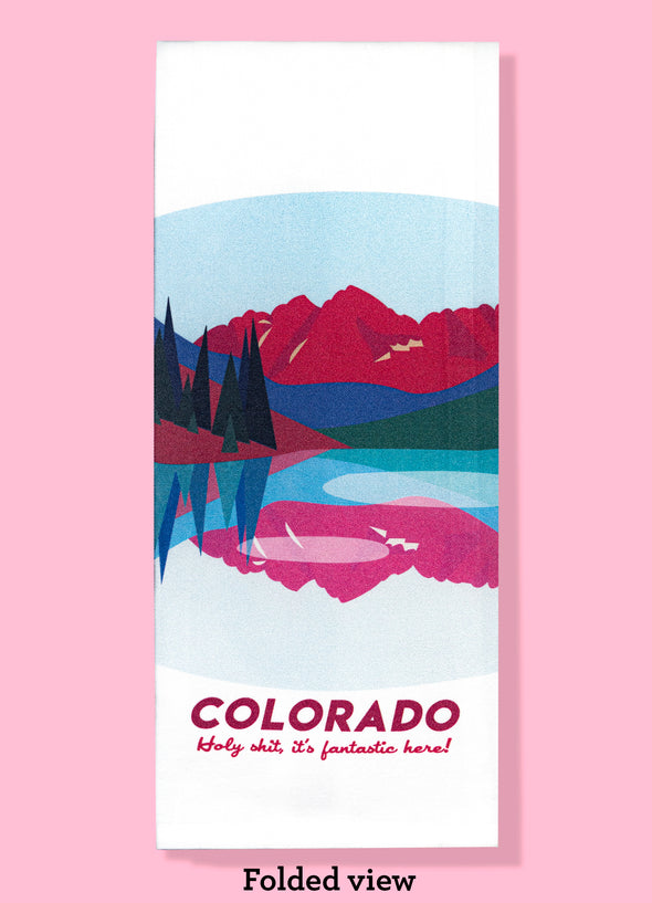 Folded dishtowel with an illustration of a lakeside landscape and the phrase Colorado Holy Shit, Its Fantastic Here.