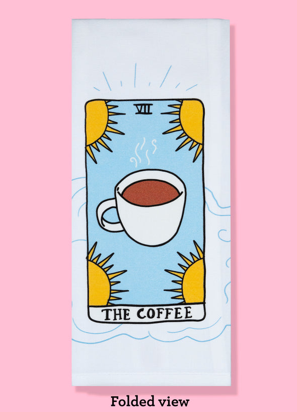 Folded dishtowel of an illustration of a faux tarot card featuring a cup filled with coffee surrounded by 4 stars with the phrase The Coffee