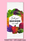 Folded dishtowel demonstrating how this product can be personalized. It features sample text that says Fuck Yes Suzanne Can Cook and an illustration of wreath of vegetables.