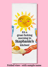 Folded dishtowel demonstrating how this product can be personalized. It features sample text that says It's a Great Fucking Morning In Stephanie's Kitchen and an illustration of a smiling sun and breakfast foods.