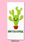 Folded dishtowel with an illustration of a smiling cactus and the phrase Don't Be a Prick.