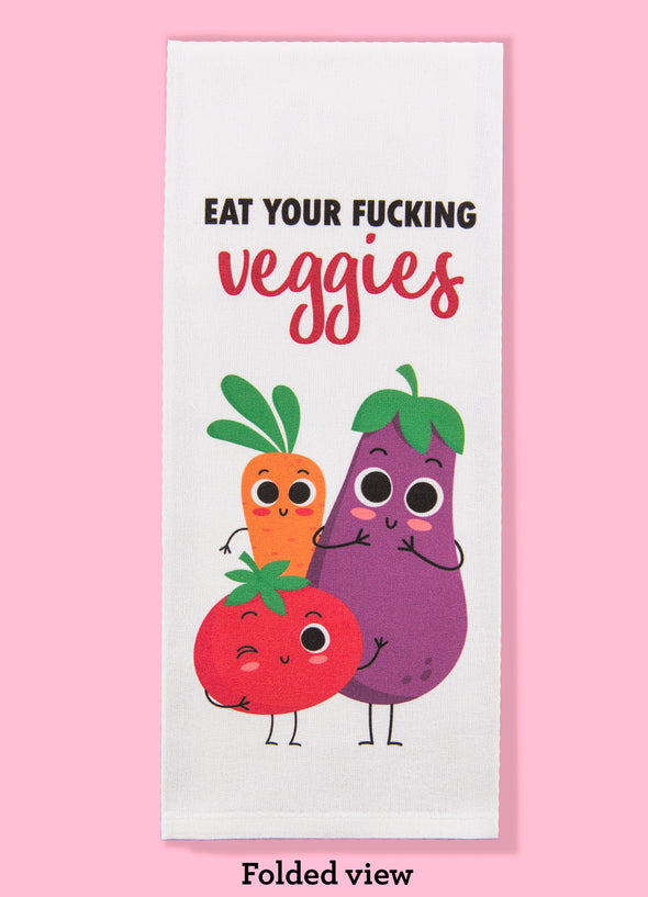Folded dishtowel with an illustration of three smiling vegetables and the phrase Eat Your Fucking Veggies.