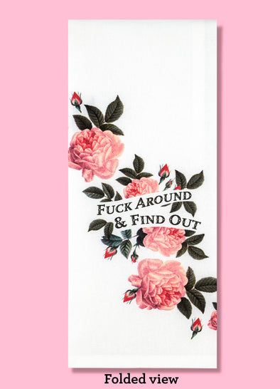 Folded dishtowel against a pink background with caption "Folded view." The dishtowel has pink vintage floral illustrations and the text Fuck Around and Find Out.