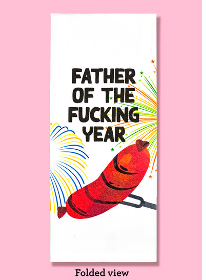 Folded dishtowel with an illustration of a hot dog and fireworks and the phrase Father of the Fucking Year.
