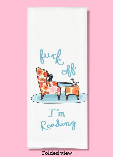 Folded dishtowel with an illustration of a person in a chair with a book and the phrase Fuck Off I'm Reading.