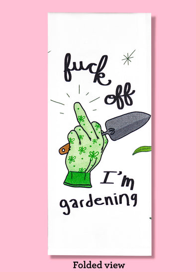 Folded dishtowel with an illustration of a gardening glove with the middle finger extended, a garden spade, and floral motifs with the phrase Fuck Off I'm Gardening.