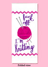 Folded dishtowel with an illustration of a ball of yarn and knitting needles with the phrase Fuck Off I'm Knitting.