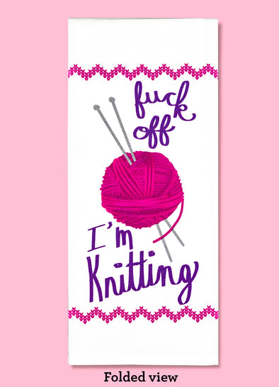 Folded dishtowel with an illustration of a ball of yarn and knitting needles with the phrase Fuck Off I'm Knitting.