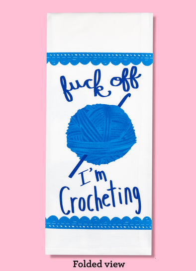 Folded dishtowel with an illustration of crochet, a ball of yarn, and a crochet hook with the phrase Fuck Off I'm Crocheting.