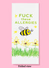 Folded dishtowel with an illustration of a bee, grass and flowers with the phrase Fuck These Allergies.