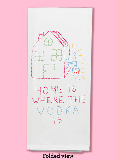 Folded dishtowel with an illustration that looks like hand stitching featuring a house with a hand sticking out of the window holding a bottle of booze and the phrase Home is Where the Vodka is.