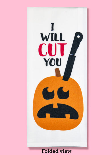 Folded dishtowel with an illustration of a massive black knife sticking into a Jack O Lantern and the phrase I Will Cut You.