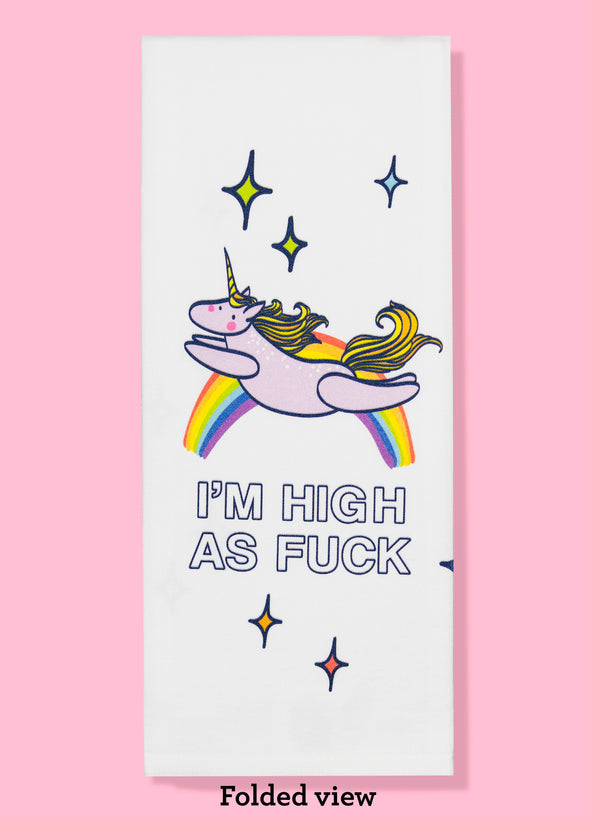 Folded dishtowel with an illustration of a unicorn leaping in front of a rainbow and the phrase I'm High as Fuck.