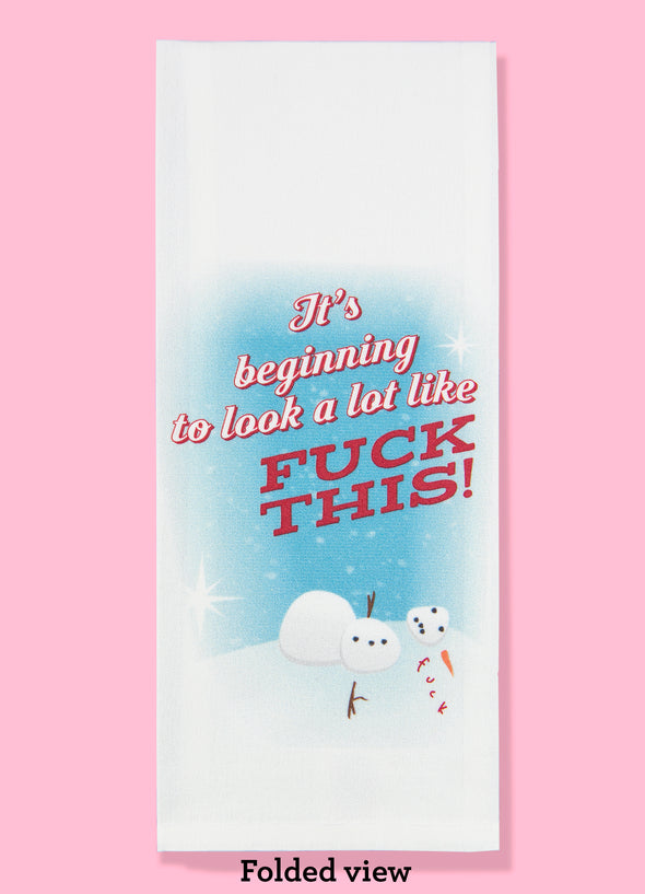 Folded dishtowel with an illustration of a fallen over snowman saying fuck and the phrase It's Beginning to Look a Lot Like Fuck This.