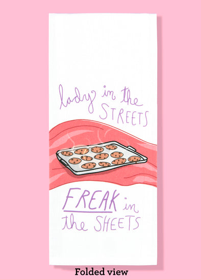 Folded dishtowel with an illustration of a pan of chocolate chip cookies on a red satin sheet and the phrase Lady in the Streets, Freak in the Sheets.