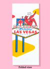Folded dishtowel of a devil sitting on top of the classic Welcome to Fabulous Las Vegas sign. The devil is saying Sin City, Baby.