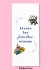 Folded dishtowel with floral illustrations and the Spanish phrase lávate las pinches manos.