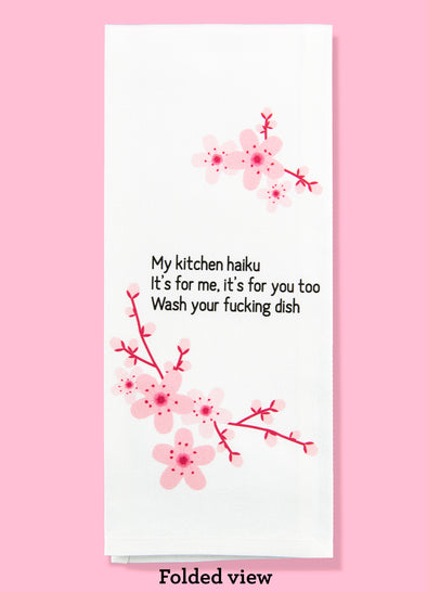 Folded dishtowel with the haiku: my kitchen haiku, it's for me it's for you too, was your fucking dish. The illustration is of cherry blossoms