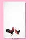 Unfolded dishtowel with an illustration of a rooster and hen facing one another. The hen has a speech line, saying nice cock.