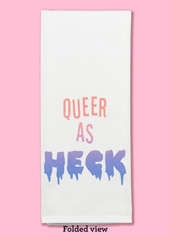  Folded dishtowel with the phrase queer as heck. The text fades from a peach color to blue.
