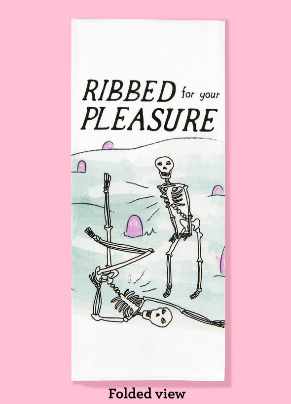 Folded dishtowel with the phrase ribbed for your pleasure. The illustration is of two cartoon skeletons in a grave yard striking sassy poses.