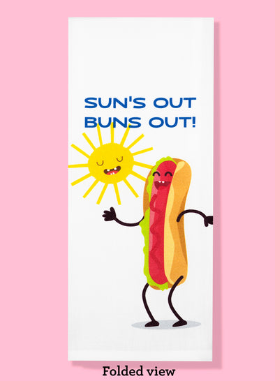 Folded dishtowel with the phrase suns out buns out and an illustration of a happy cartoon hotdog and sun
