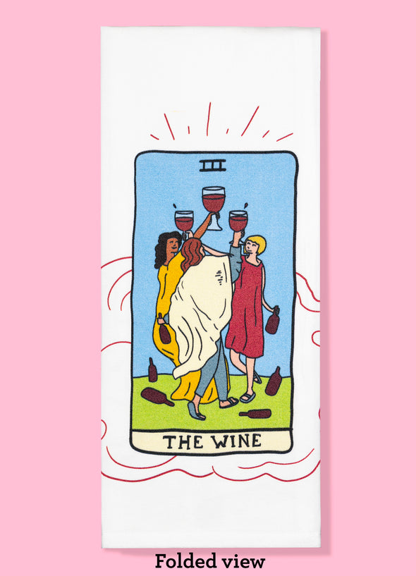 Folded dishtowel of an illustration of a faux tarot card featuring women dancing and holding glasses of wine with the phrase The Wine