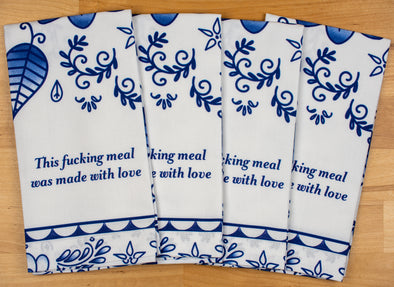 A complete set of four identical napkins. They read this fucking meal was made with love. They are all folded in the same manner of the same design. 