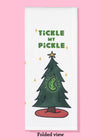 Folded dishtowel of an illustration of a Christmas tree with a large pickle ornament with the phrase tickle my pickle