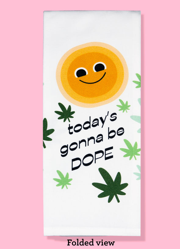 Folded dishtowel with the phrase today's gonna be dope. The illustration features a cartoon sun with eyes and a smiling face surrounded by cartoon marijuana leaves