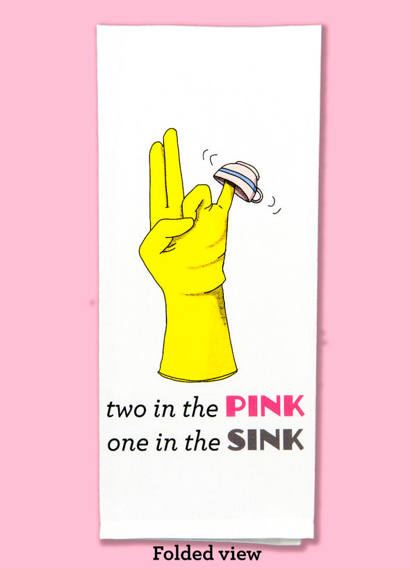 Folded view of the two in the pink, one in the sink dishtowel. This dishtowel features a rubber glove with index and and middle finger together and extended, the ring finger and thumb touching, and the pinky extended to the side with a tea cup on it, as well as the humorous phrase.