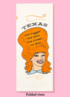 Folded dishtowel with the phrase Texas the bigger the hair, the closer to God. The illustration is of a cartoon smiling woman with large red hair.