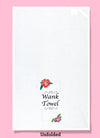 unfolded dishtowel with the phrase wank towel. The text is surrounded by illustrations of flowers in the upper left and lower right of the design and black squiggles in the upper right and lower left