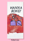 Folded dishtowel with the phrase wanna bone? The illustration is of a skeleton reclining on two purple gravestones on a red watercolor hill