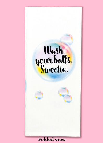 Folded dishtowel with the phrase wash your balls, sweetie. The text is in an illustration of bubbles. 