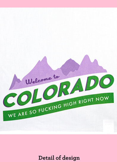  A closeup view of the design of welcome to Colorado we are so fucking high right now. The illustration is purple mountains with weclcome to on it. The rest of the text is in green below the mountains.